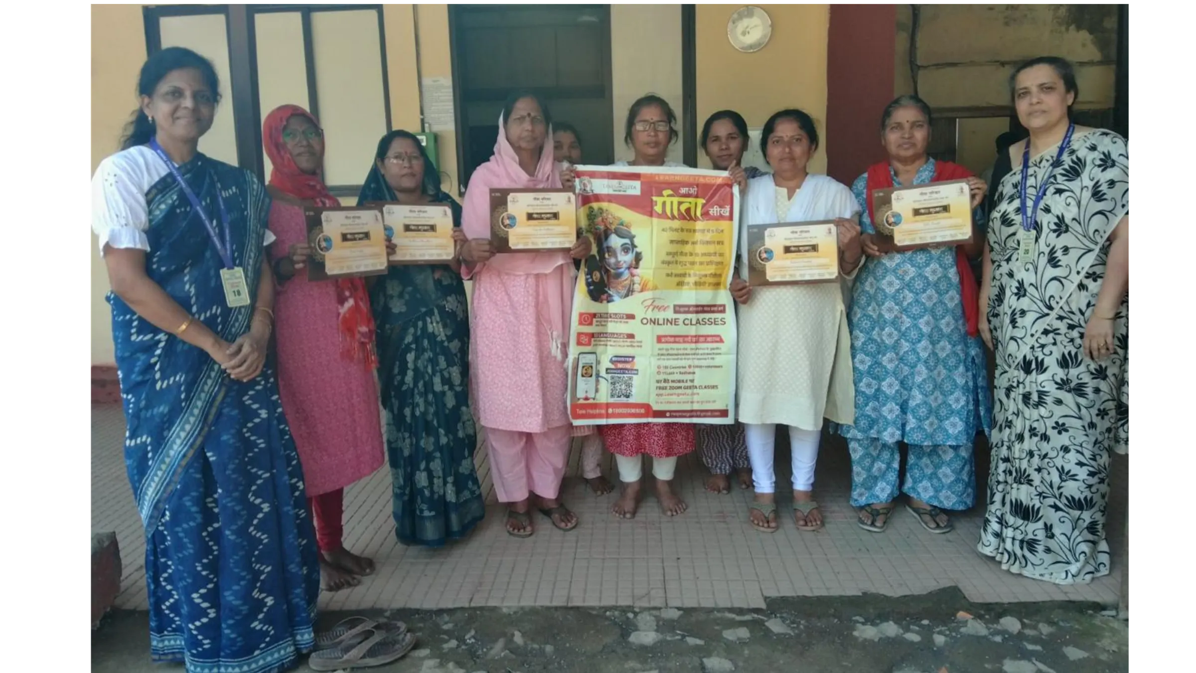 गीता पाठ्यक्रम पूर्ण करने वाली महिलाएँ प्रमाणपत्र और 'आगे गीता सीखें' पोस्टर के साथ संस्थान परिसर में।